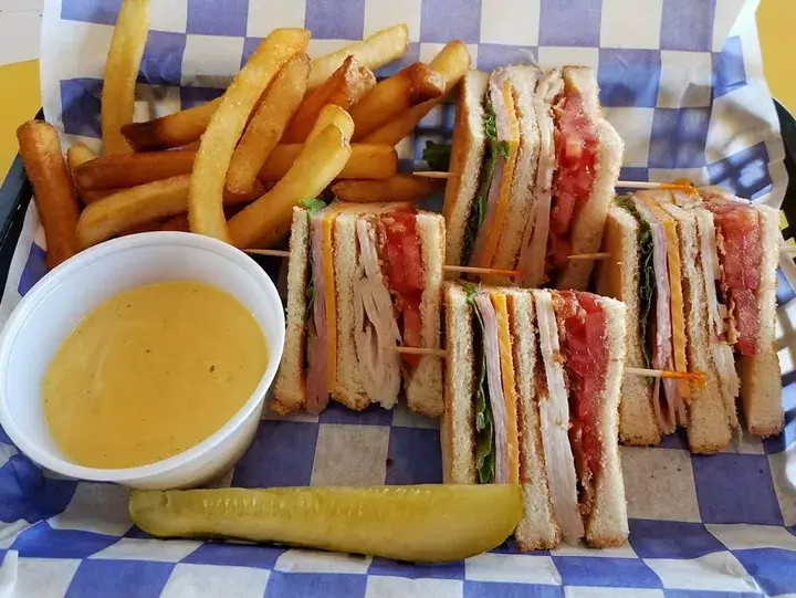 A towering triple-decker club sandwich stacked with layers of roasted turkey, crispy bacon, fresh lettuce, juicy tomato slices, and creamy mayo, all between three slices of toasted bread.