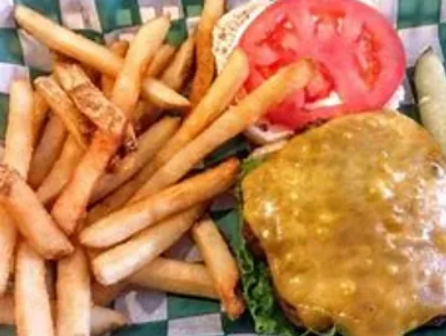 A juicy cheeseburger with a melted slice of cheddar cheese, fresh lettuce, tomato, and pickles, served on a toasted bun alongside a generous portion of golden, crispy fries.